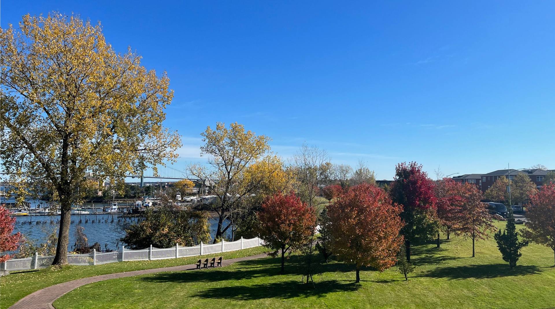 Powell Cove Estates waterfront lawn and autumn trees along the cove in College Point, Queens, with the Whitestone Bridge in the distance